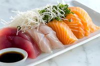 Fresh sashimi assortment with tuna, white fish, and salmon served on white plate with soy sauce and daikon radish sprouts, traditional Japanese cuisine.