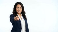 Professional Hispanic businesswoman in navy suit pointing at camera with confident smile on white background for corporate presentations.