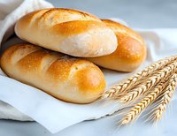 Fresh baked golden bread rolls on white cloth with wheat ears, close up view of crusty homemade buns showing soft texture and natural ingredients.