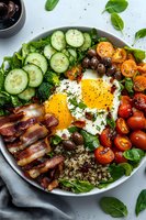 Fresh breakfast bowl with sunny side up egg, crispy bacon, quinoa, cucumber slices, cherry tomatoes, olives and spinach leaves on white ceramic plate.