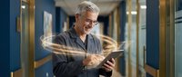 Senior Caucasian businessman using digital tablet with glowing light trails in modern office corridor, representing connectivity and innovation in workplace.