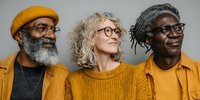 Diverse senior friends in yellow outfits and glasses looking thoughtfully to the side, representing community, wisdom, and modern aging.