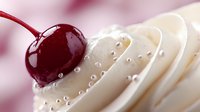 Fresh red cherry with water drops resting on swirled white cream, creating luxurious dessert garnish with soft pink bokeh background for food photography.