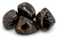 Polished black marble stones with golden veins on white background, smooth tumbled rocks showing natural mineral patterns and textures in dark glossy surface.