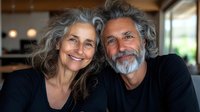 Happy mature couple with gray hair smiling together in modern home interior. Senior man and woman embracing, showing love and companionship in retirement years.