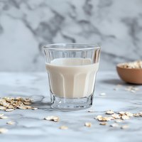 Fresh oat milk in glass on marble background with scattered oats, dairy alternative beverage for healthy lifestyle and plant-based diet.