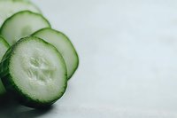 Fresh cucumber slices arranged on light background showing translucent texture and crisp detail, minimalist food composition for healthy eating concepts.