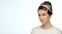 Young woman with elegant updo hairstyle wearing decorative headband and cream sweater against white background for fashion and beauty concepts.