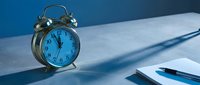 Vintage brass alarm clock showing midnight on white desk with notebook and pen in blue lighting for time management and productivity concepts.