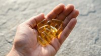 Caucasian hand holding golden omega-3 fish oil capsules against marble background, representing dietary supplements, wellness, and nutritional health for medical and lifestyle content.