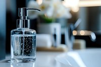 Clear glass soap dispenser with bubbles on bathroom counter against blurred background with soft bokeh lights and minimalist aesthetic.