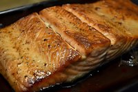 Grilled salmon fillets with golden caramelized surface in cast iron skillet, seasoned with herbs and spices for gourmet seafood cooking and healthy dining.
