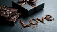 Dark chocolate bar with cocoa shavings and gift box on slate, with the word Love written in cocoa powder for Valentine's Day.