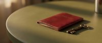Red leather journal with gold clasp resting on round table surface, suitable for stationery, office, and lifestyle design projects.