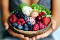 Fresh mixed berries and fruits in wooden bowl with lettuce garnish held in feminine hands, shallow depth of field focus on vibrant seasonal produce.