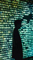 Silhouette of male figure against glowing digital binary code wall in green and blue tones, representing cybersecurity and data technology concepts.