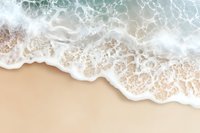 Aerial view of ocean waves washing up on sandy beach with white foam creating natural patterns. Turquoise water meets beige sand in serene coastal scene.