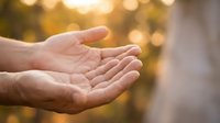 Open cupped hands reaching upward in warm golden sunlight with soft bokeh background creating peaceful spiritual moment for meditation and prayer concepts.