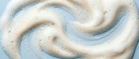 Creamy white foam swirls create elegant spiral patterns on light blue surface for skincare cosmetics and beauty product backgrounds.