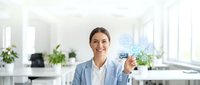 Woman in business casual attire holding digital holographic interface with technology icons in modern office environment for corporate and innovation concepts.