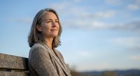 Mature Caucasian woman with gray hair enjoying peaceful moment outdoors against blue sky, representing wellness, retirement lifestyle and positive aging.