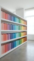 Modern home library with rainbow colored books arranged by hue on white floating shelves creating vibrant gradient display in minimalist interior.