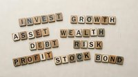 Financial terms spelled with wooden letter tiles on linen background, featuring invest, growth, wealth, debt, risk, profit, stock, bond concepts.