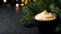 Creamy eggnog in black bowl with Christmas tree branches and warm bokeh lights creating festive holiday atmosphere for seasonal celebrations and winter traditions.