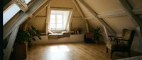 Spacious attic room with wooden beams, skylight window, hardwood flooring, and potted plants. Suitable for loft conversions, interior design, and home renovation projects.