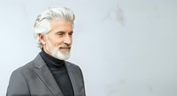 Mature man with white hair and beard wearing gray blazer and black turtleneck against white background. Professional portrait for business, corporate, and lifestyle design projects.
