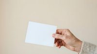 Close-up of hand holding blank white card against neutral beige background, suitable for mockups, branding, and business presentations.