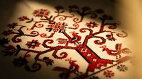 Traditional folk embroidery with red and black cross-stitch tree of life pattern on white linen fabric, warm light.