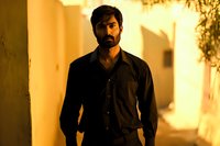 Middle Eastern man with beard wearing dark shirt standing in dramatic golden light with shadows on wall, creating mysterious atmospheric mood for cinematic portraits.