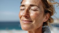 Mature Caucasian woman with freckles enjoying sunshine at beach, eyes closed with peaceful expression, natural beauty and wellness concept.