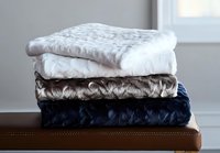 Stack of luxurious textured blankets in white, beige and navy blue colors folded neatly on brown leather surface, soft cozy home decor arrangement.