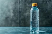 Clear plastic bottle with sparkling water and yellow cap on blue textured surface against dark moody background, showing condensation droplets and freshness.