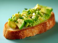 Fresh sliced avocado on crispy toasted bread garnished with herbs and seasonings against turquoise background, macro food photography for healthy eating.