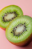 Fresh sliced kiwi fruit showing detailed inner texture and seeds on pink background, macro photography highlighting natural patterns and vibrant colors.
