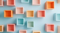 Colorful geometric boxes in coral, mint and orange shades arranged on light blue wall creating modern minimalist pattern with soft shadows and depth effect.