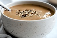 Creamy chocolate smoothie bowl topped with crunchy cacao nibs and sesame seeds in speckled ceramic bowl, close up view on light background.