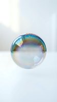Iridescent soap bubble floating against clean white background with rainbow reflections and transparent surface for design projects.