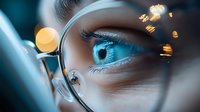 Close-up macro shot of bright blue eye seen through eyeglass lens with golden bokeh lights creating magical atmosphere, selective focus on iris and lashes.