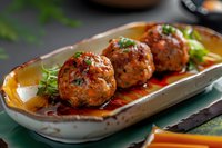 Juicy meatballs with herbs and spicy sauce served on ceramic plate. Close up view of homemade appetizer garnished with fresh greens and sauce.
