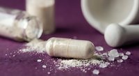 Pharmaceutical capsules with white powder spilled on purple surface. Medical supplements and pills for healthcare treatment and wellness therapy.