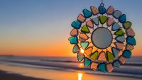 Colorful stained glass sun catcher with vibrant petals against golden sunset beach backdrop creating peaceful meditation and spiritual wellness atmosphere.