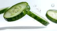 Fresh cucumber slices with water drops floating in air against white background, healthy organic vegetable for salad and skincare concept.