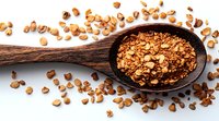 Wooden spoon filled with crunchy granola mix and scattered nuts on white background, macro food photography for healthy breakfast and snack concepts.