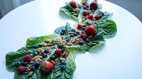 Festive holiday table runner made from fresh green leaves decorated with cranberries, blueberries, nuts and berries for Christmas dinner centerpiece.