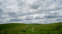 Rolling green hills with lush grass under dramatic cloudy sky, suitable for landscape, nature, and environmental design projects.