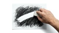 Hand erasing pencil scribbles with white eraser on paper, removing dark graphite marks. Creative process of correction and artistic editing concept.